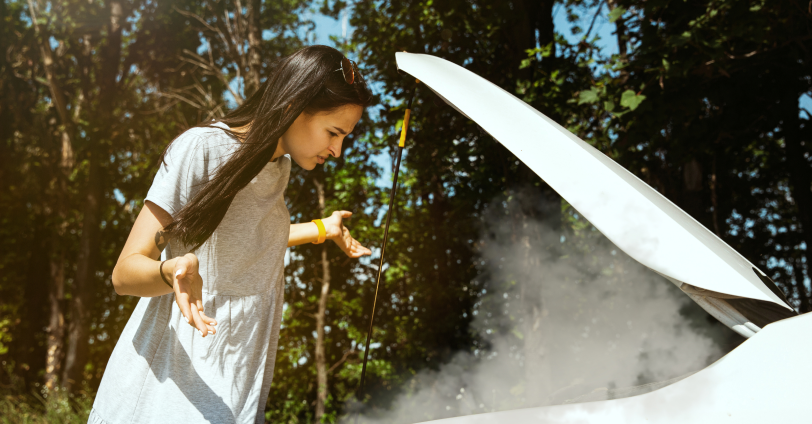 A distressed woman in front of a smoking open car bonnet.