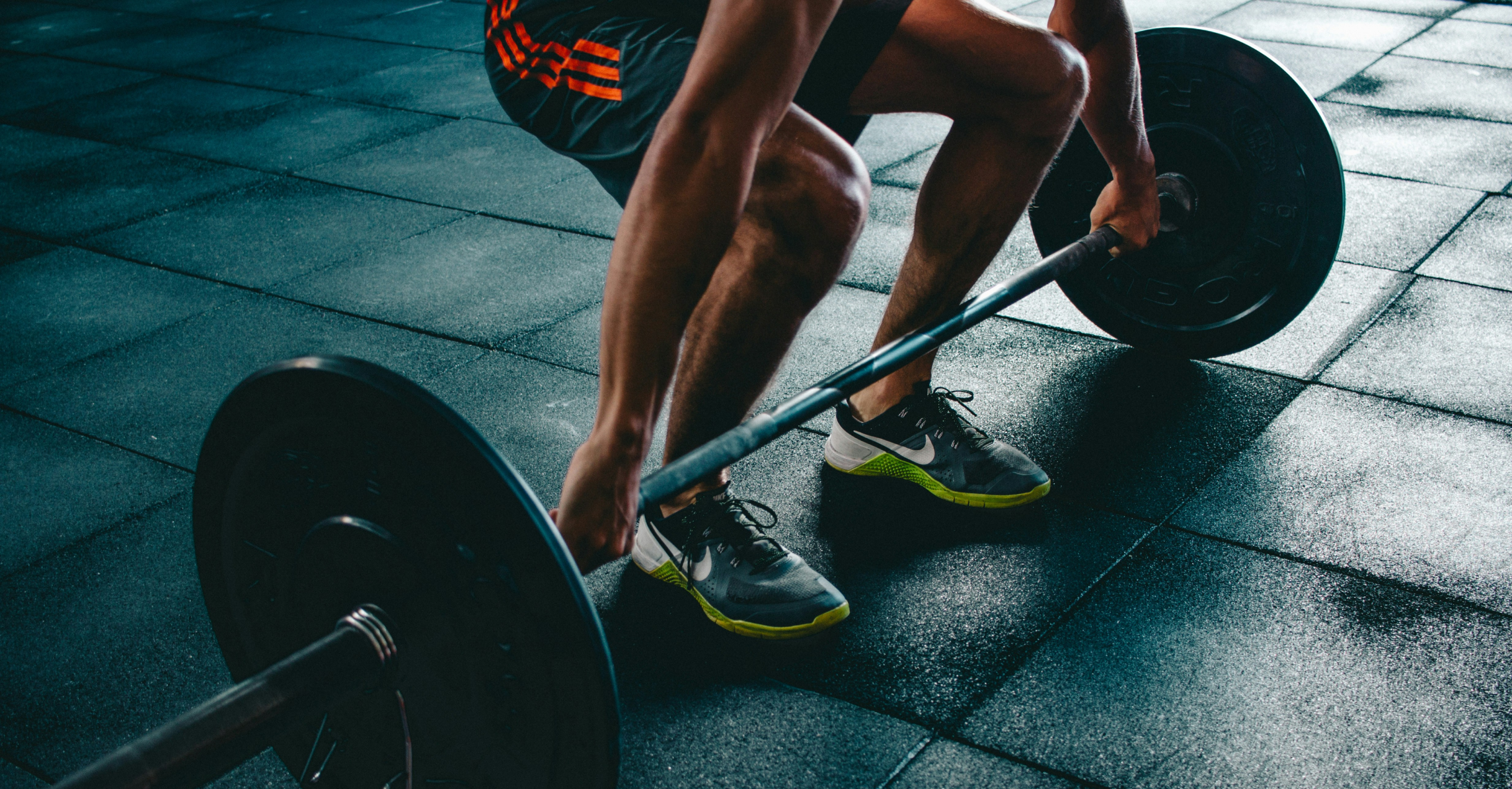 A person wearing sport shoes lifting a set of weights.