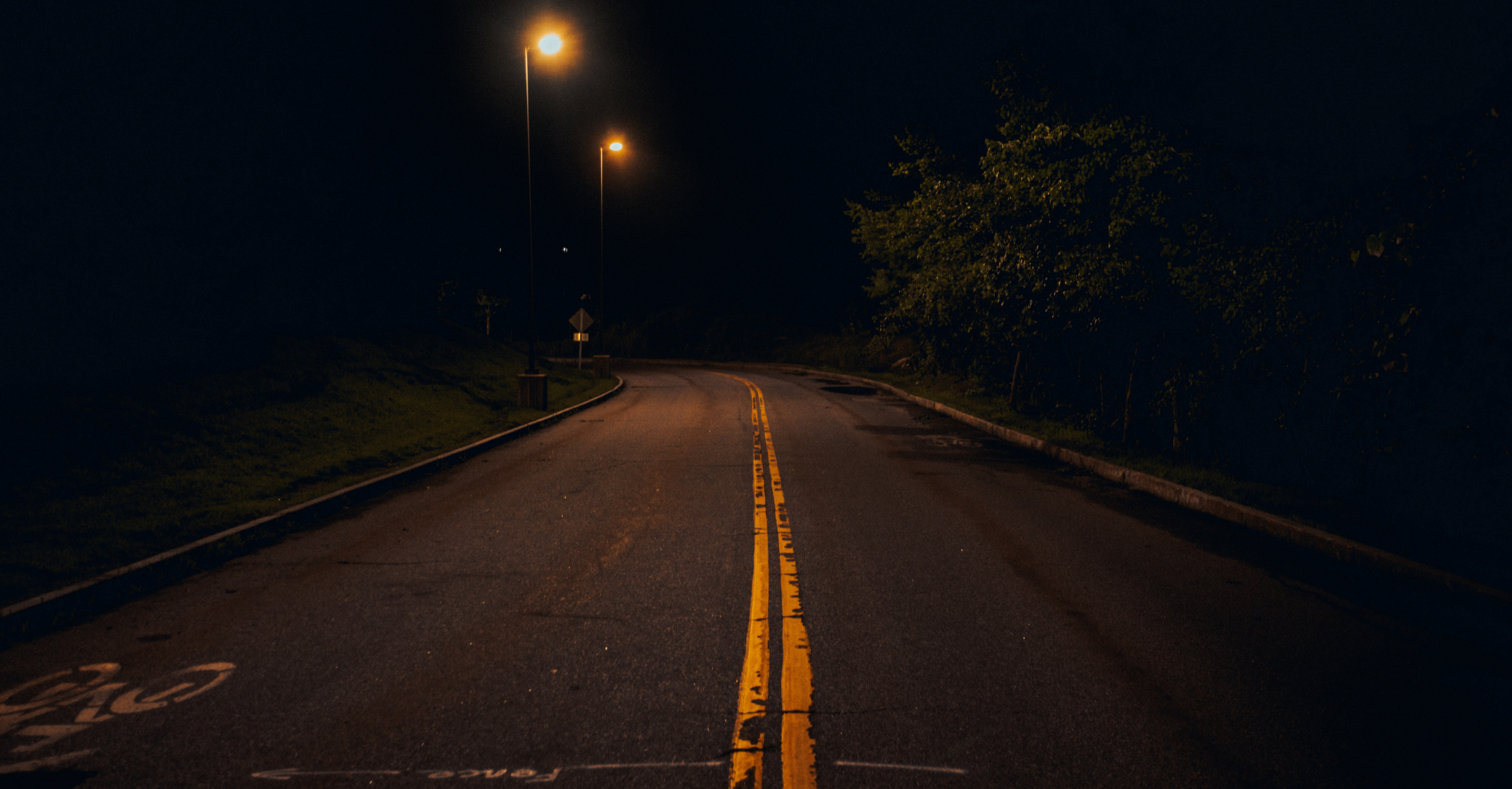 An Empty Road With Yellow Lines At Night.